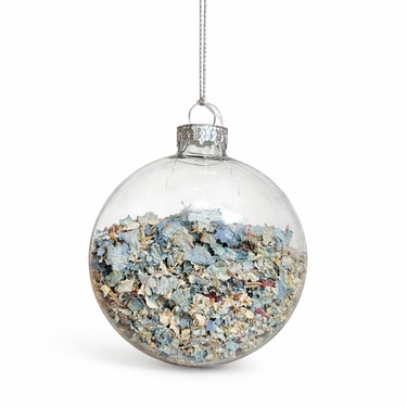 Clear glass Christmas ornament filled with blue and beige decorative stones on a white background