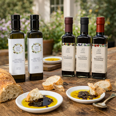 Bottles of olive oil and balsamic vinegar on a wooden table with bread and dips.