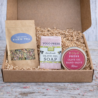 Box containing Yolo Press soap and olive oil salve with a Farm Tea package on a wooden surface.